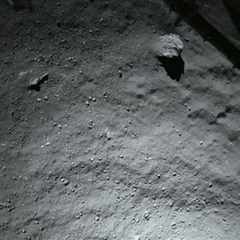 Die Kometenoberfläche, aufgenommen aus etwa 40 m Höhe mit dem nach unten schauenden Kamerasystem ROLIS. Die Oberfläche ist bedeckt mit Staub und Steinen im Größenbereich von einigen mm bis m. Der große Block in der oberen rechten Ecke ist etwa 5 m groß. In der gleichen Ecke ist ein Teil eines Landebeins von Philae zu sehen.
(Bild: ESA/Rosetta/Philae/ROLIS/DLR)