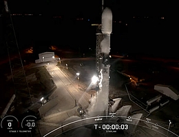Falcon 9 steht wenige Sekunden vor dem Start auf dem Pad. Die unter der Rakete zu sehenden Wasserfontänen sind Teil des Schallunterdrückungssystems, das Auswirkungen des beim Start auftretenden Schalldrucks abmildern soll. (Bild: Webcast SpaceX)