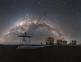 Der dunkle Himmel über dem Paranal-Observatorium der ESO, in dem das Very Large Telescope (VLT) der ESO untergebracht ist, bietet atemberaubende Ausblicke, die so klar und voller Sterne sind, dass man sie fast berühren könnte. Auf einer Plattform des VLT stehend, streckt ESO-Fotobotschafter Petr Horálek seine Hand nach einem auffälligen Objekt am Himmel aus. Man könnte diesen hellen Körper, wie viele andere am Himmel, für einen Stern halten, aber in Wirklichkeit handelt es sich um einen Planeten in unserem Sonnensystem: den Gasriesen Jupiter. Näher an der Erde sind im Hintergrund die vier Unit Telescopes (UTs) zu sehen, aus denen das VLT besteht. Jedes UT verfügt über einen 8,2-Meter-Spiegel, und im Zusammenspiel sorgen sie für einen der schärfsten Blicke auf das Universum. Die vier UTs werden von vier kleineren, beweglichen Hilfsteleskopen (ATs) begleitet, die über 1,8-Meter-Spiegel verfügen. Die chilenische Atacama-Wüste beweist einmal mehr ihren Wert als idealer Standort für das VLT der ESO. Die Abgeschiedenheit des Observatoriums bedeutet, dass es nur sehr wenig bis gar keine Lichtverschmutzung gibt, was für die Astronomie von entscheidender Bedeutung ist und zudem atemberaubende Ausblicke ermöglicht. Ein Himmelsbogen zum Anfassen. (Bild: ESO