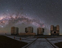Kosmischer Regenbogen über dem VLT Dieses ausgefallene Bild der Woche wurde vom Paranal-Observatorium der ESO aus aufgenommen. Der Standort des Very Large Telescope liegt auf einer Höhe von stolzen 2635 Metern, auf dem Gipfel des Cerro Paranal in der nördlichen Atacama-Wüste. Die vier Hauptteleskope des VLT, etwas rechts der Mitte auf diesem Panorama, posieren vor dem ausgedehnten Bogen der Milchstraße, die fast wie ein Regenbogen aus Sternen aussieht. Man erkennt auf dem Bild auch drei der vier Hilfsteleskope. Die Astronomen verwenden unterschiedliche Konfigurationen dieser Hilfsteleskope, die auf Schienen über die Plattform hinweg verfahrbar sind. Können Sie alle drei Hilfsteleskope auf dem Bild ausmachen? Bildnachweis: ESO/P. Horálek